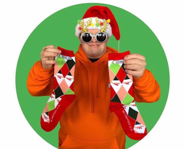 Ross From Stand Out Socks Wearing a Santa Hat & Funny Glasses Holding up a pair of stand out Christmas socks