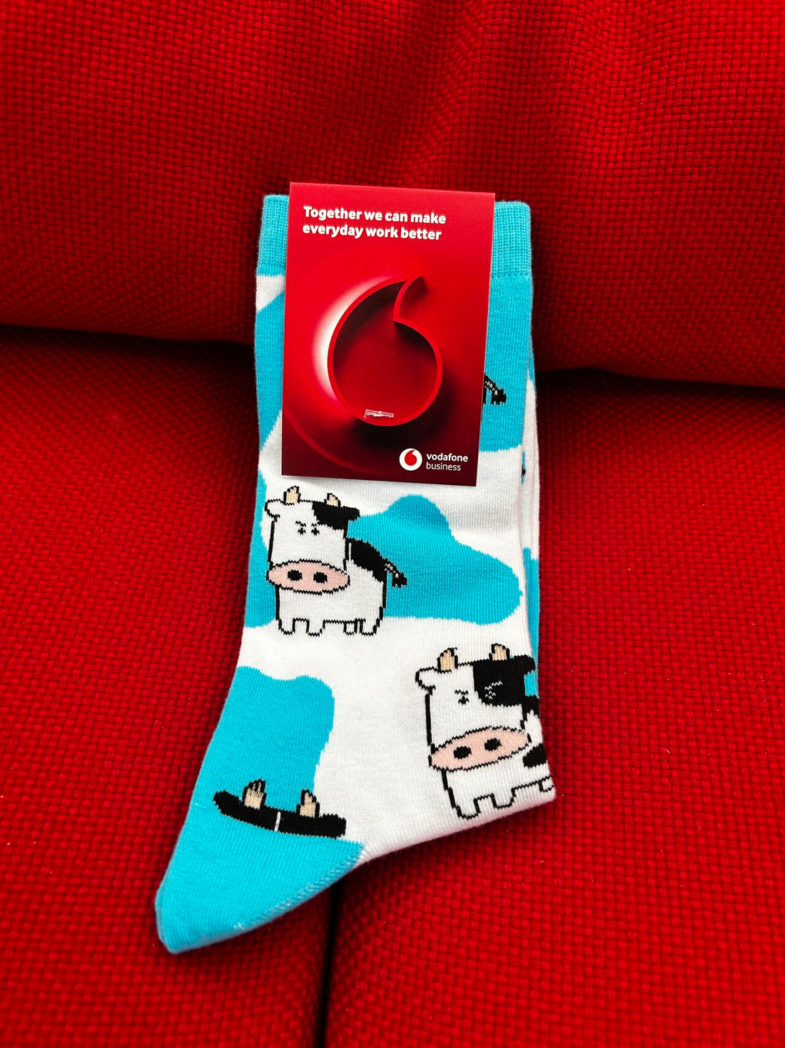 A pair of stand out socks with a cow print and cow design with a Vodafone sock tag