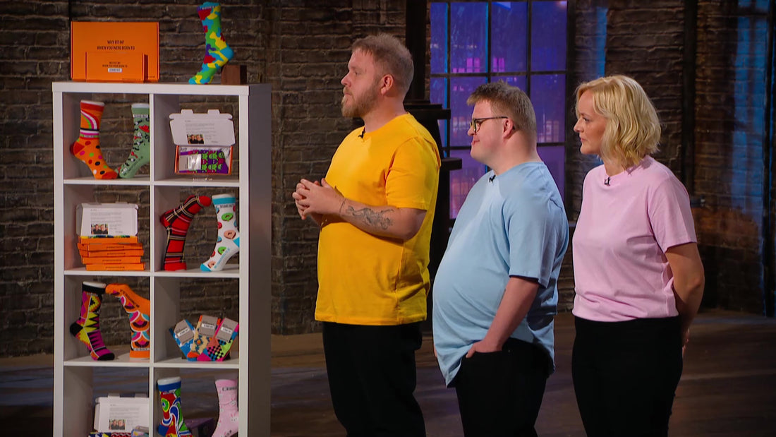 2 Men and a Woman dressed in brightly coloured tshirts stood next to some bright and funky stand out socks 