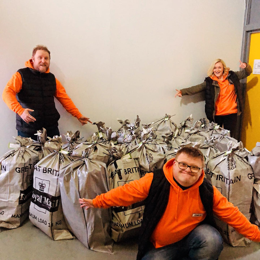 2 men and a woman next to lots of royal mail postage bags