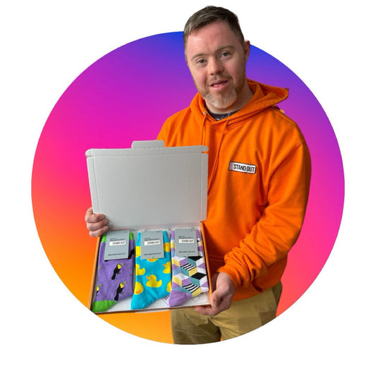 A Man wearing an orange hoodie, holding up a box of colourful socks. There is a pink and purple circle frame around the photo