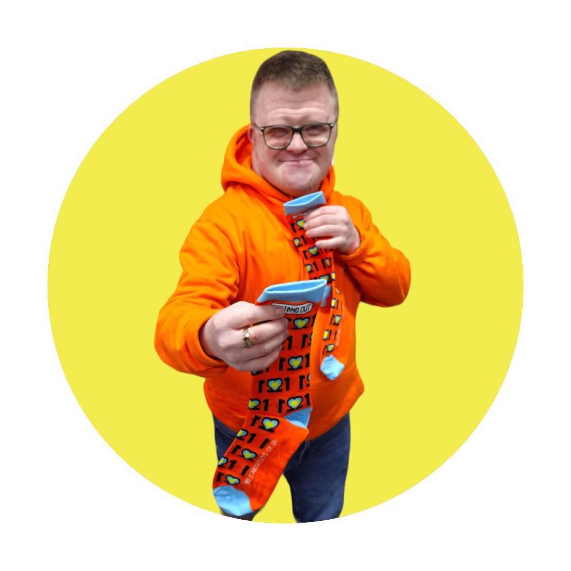 Man with Glasses on and orange jumper, Smiling and holding a pair of colourful Down Syndrome Awareness Socks