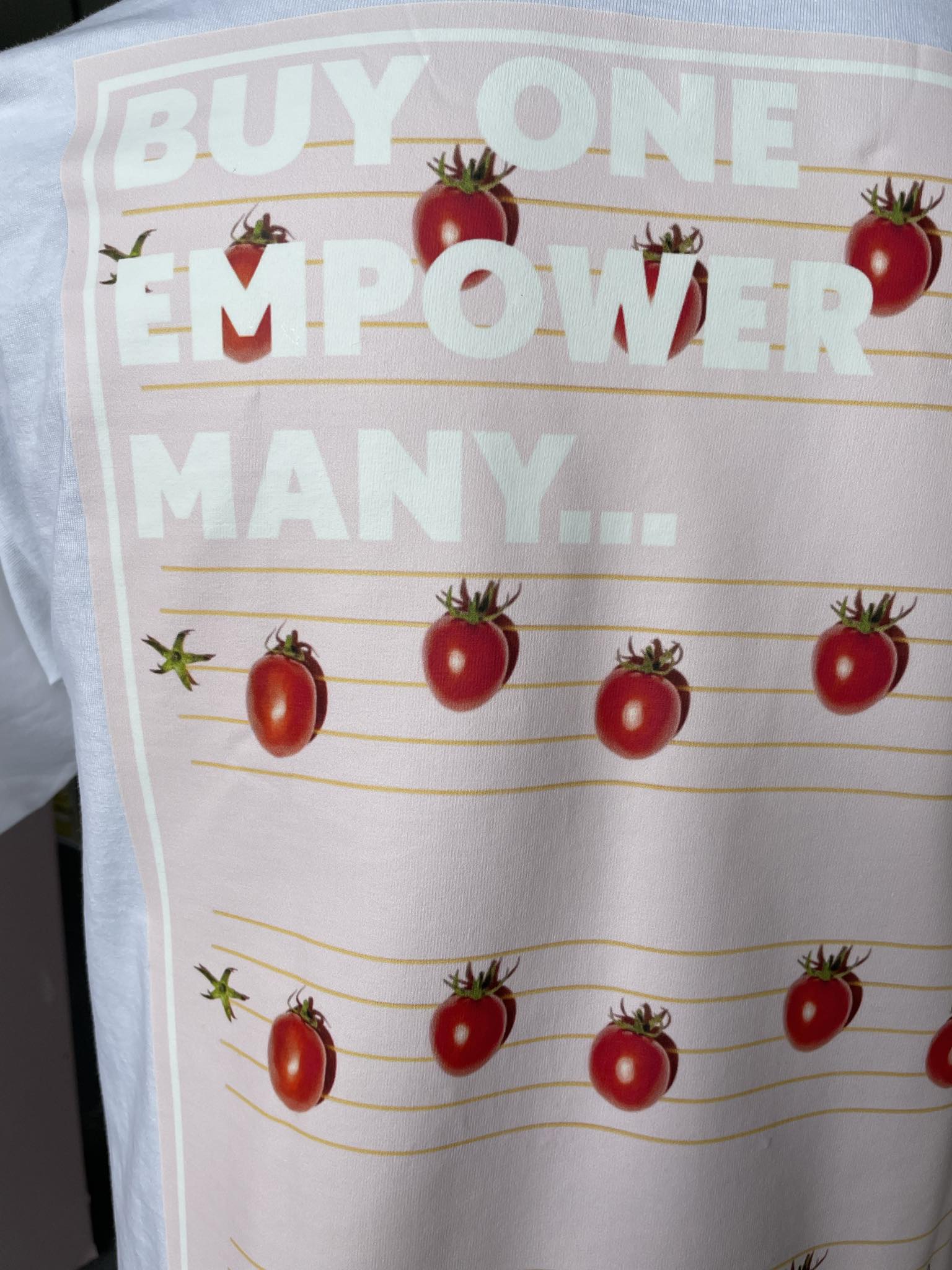 Close up of Stand Out Socks White T-shirt with tomato's patten print and the words buy one, empower many on the back.