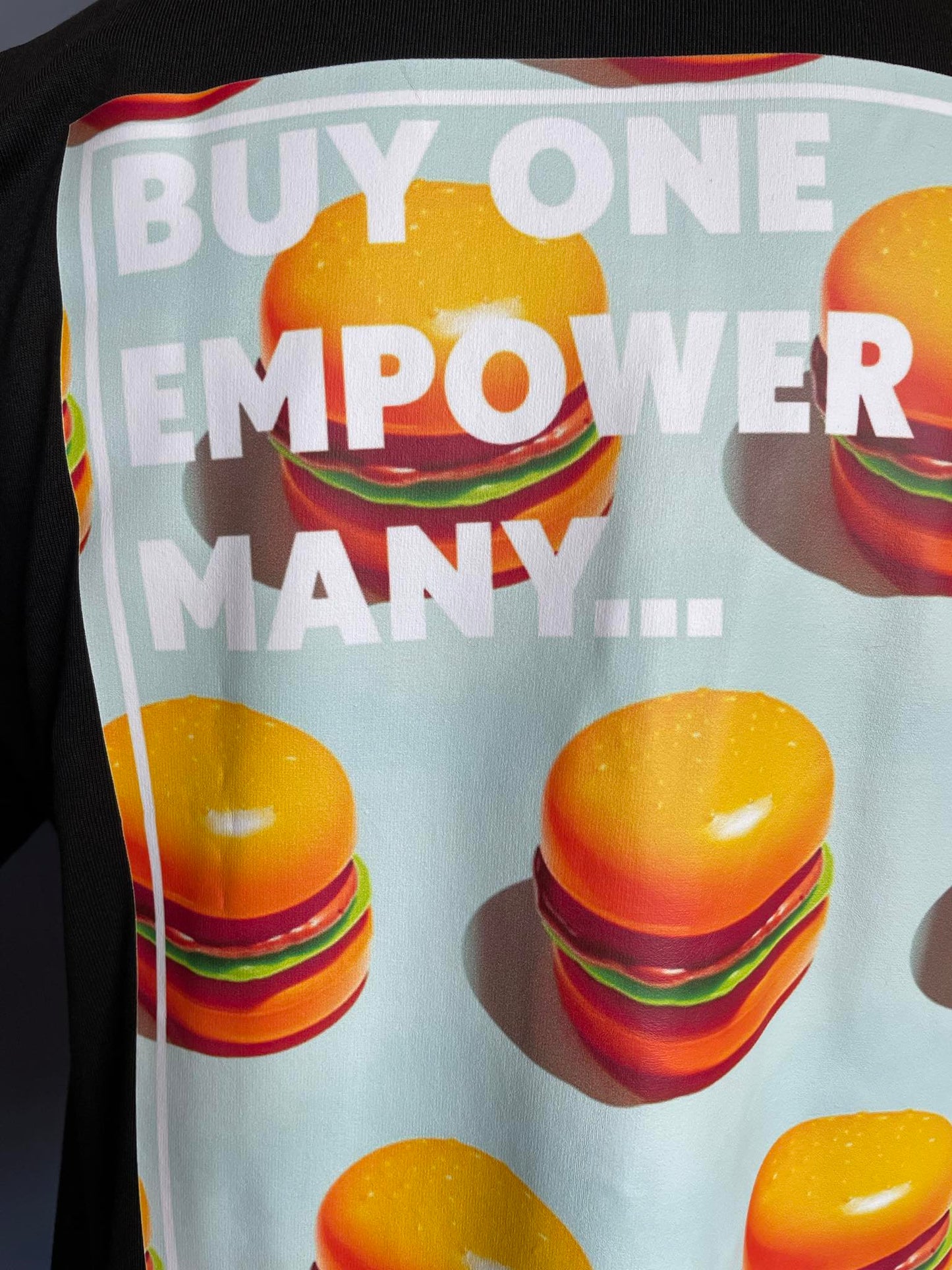 Stand Out Socks Black Tshirt with Burger patten print and the words buy one, empower many on the back.