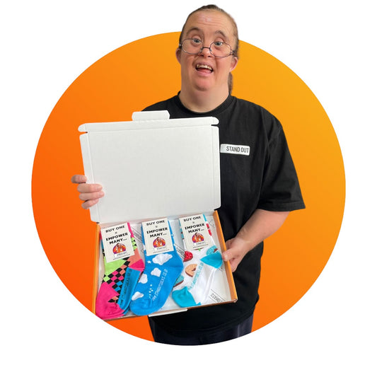 A lady with Down Syndrome proudly holding up an orange box containing 3 pairs of Stand Out kids socks with clouds, donut and 90s retro patterns.