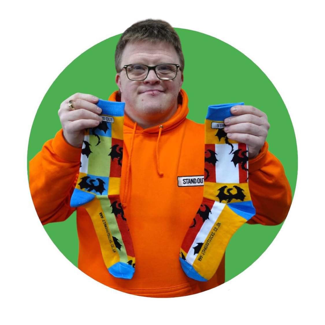 A Man who has Down Syndrome holding up a pair of stand out socks which have coloublocs and dragons den dragon pattern