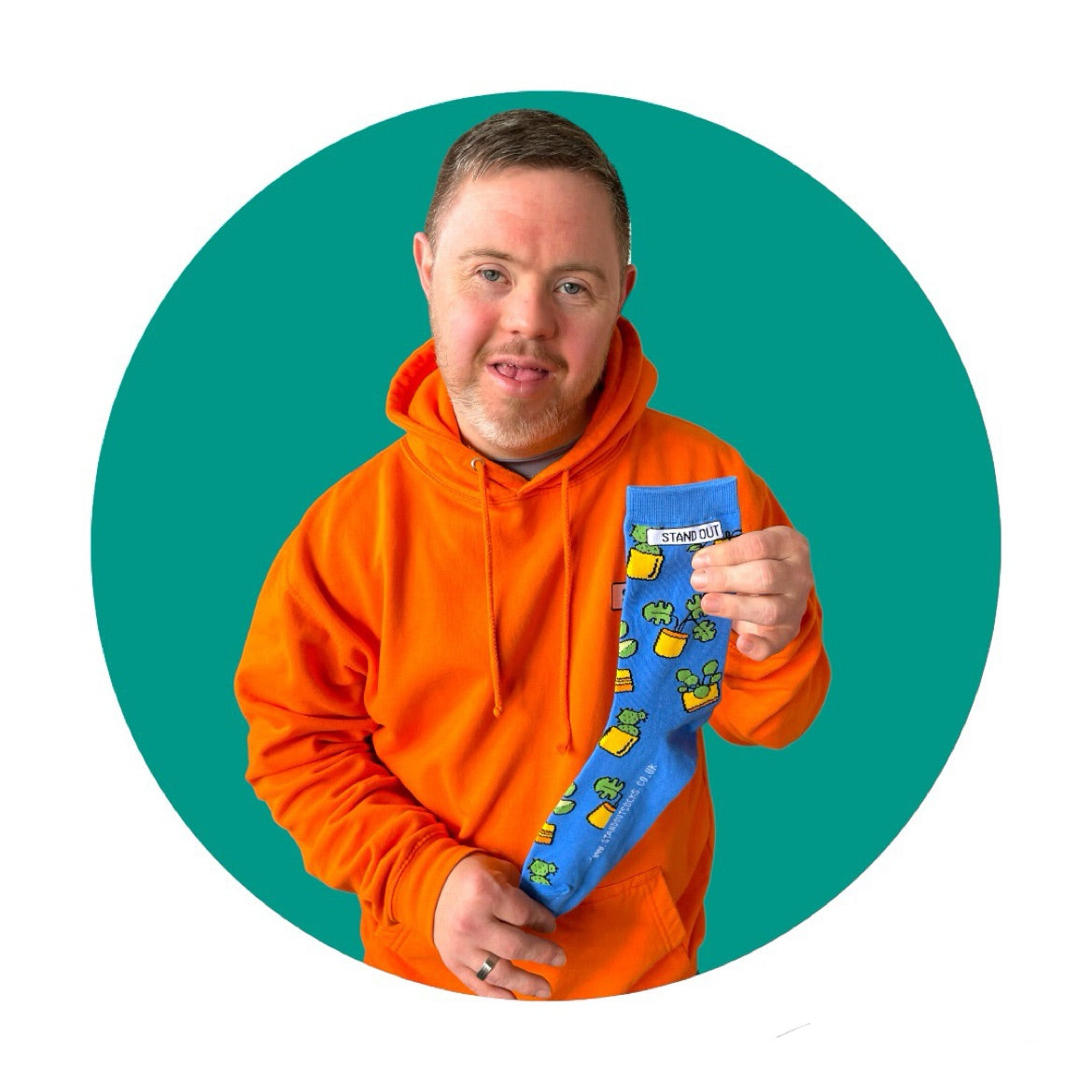 A man who has down syndrome holding up a pair of blue socks with a design of plants in pots. The picture has a green circle frame around it.,