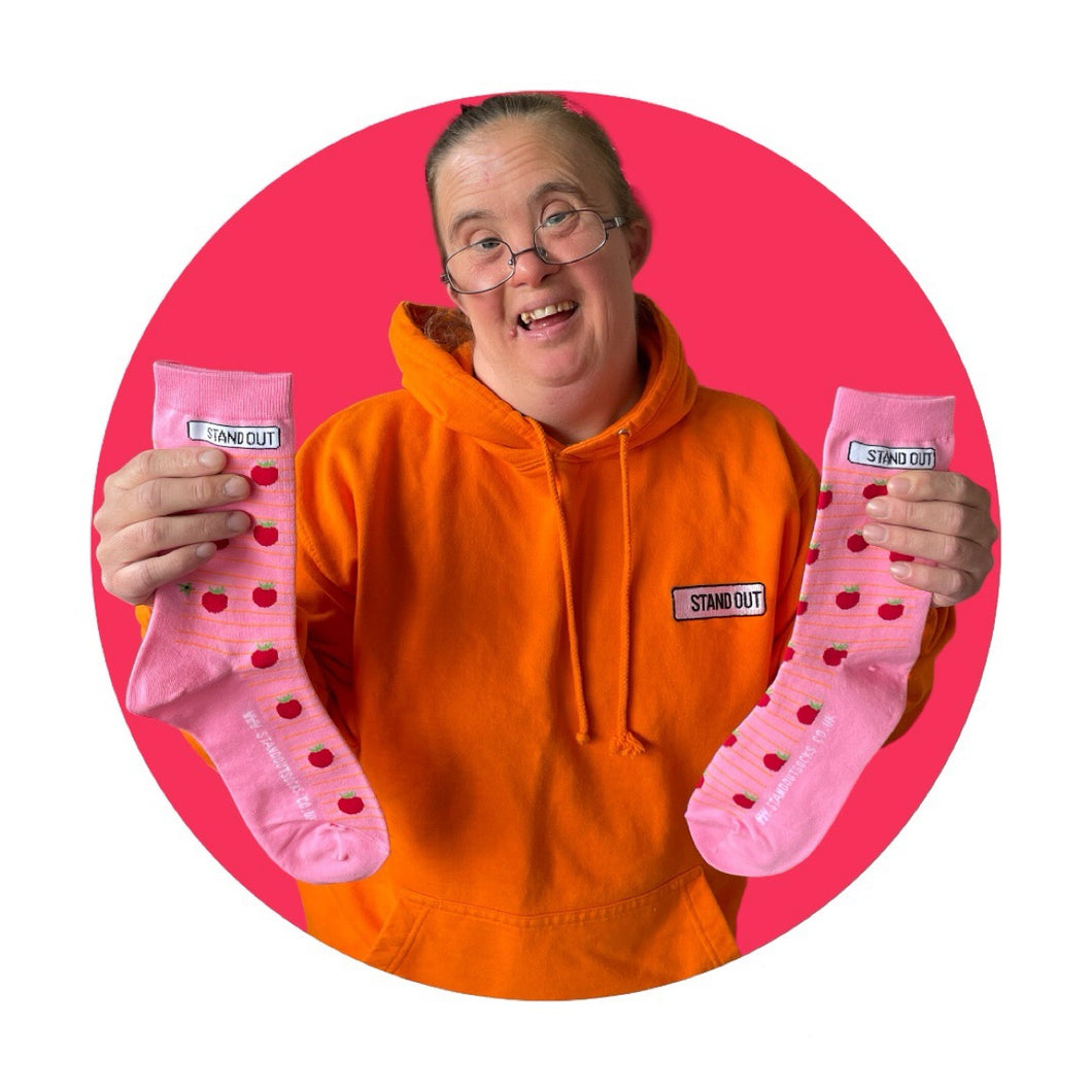 Lady with orange jumper on holding up a pair of pink socks with tomato pattern, surrounded by a pink circle border.