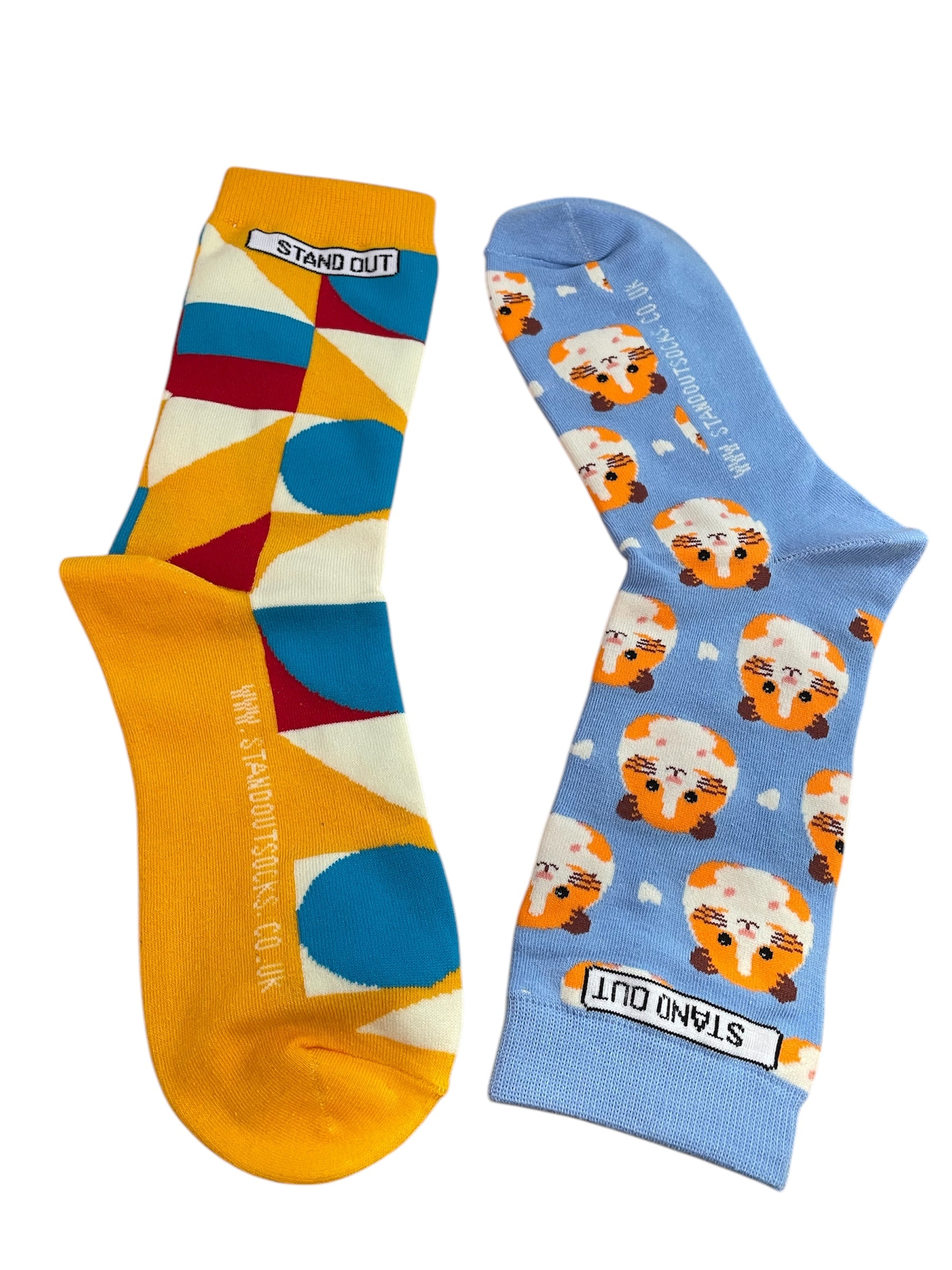 A Pair of Odd Socks, One sock is orange with Geometric design, one sock is blue with hamsters. Both socks display the STAND OUT logo on the ankle, and wwww.standoutsocks.co.uk website on the ball of the foot.