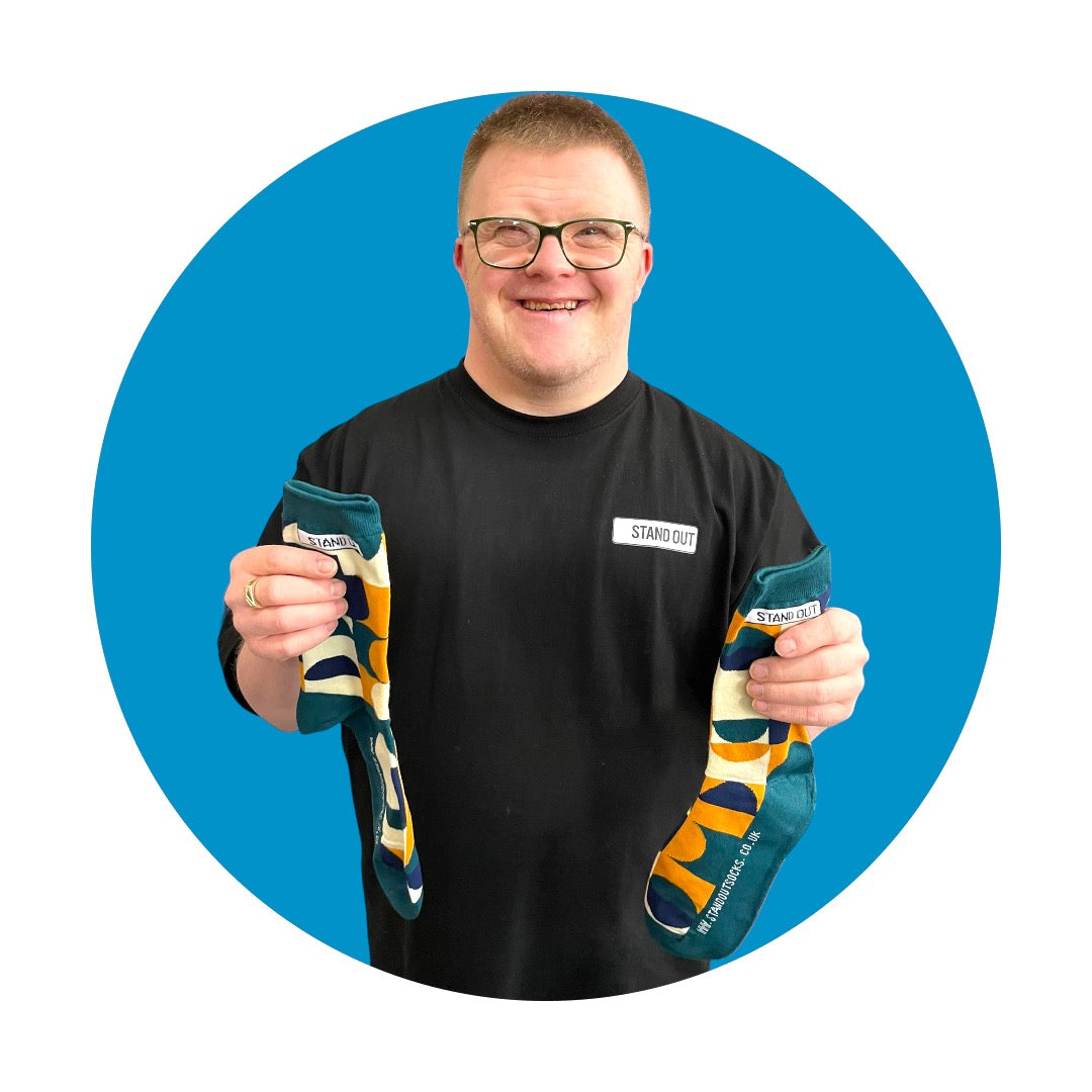 A Man holding up a pair of Geometric Patterned socks and smiling. There is a Blue circle frame around the picture. 